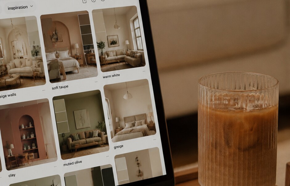 Laptop op een houten tafel met een interieur-moodboard vol beige, taupe en greige tinten op het scherm, naast een glas ijskoffie.