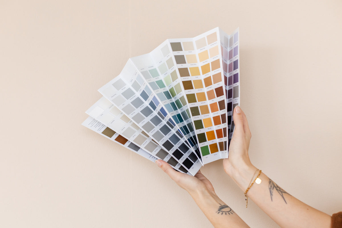Hand houdt een waaier met verfstalen voor een wand om de kleur in verschillend licht te beoordelen