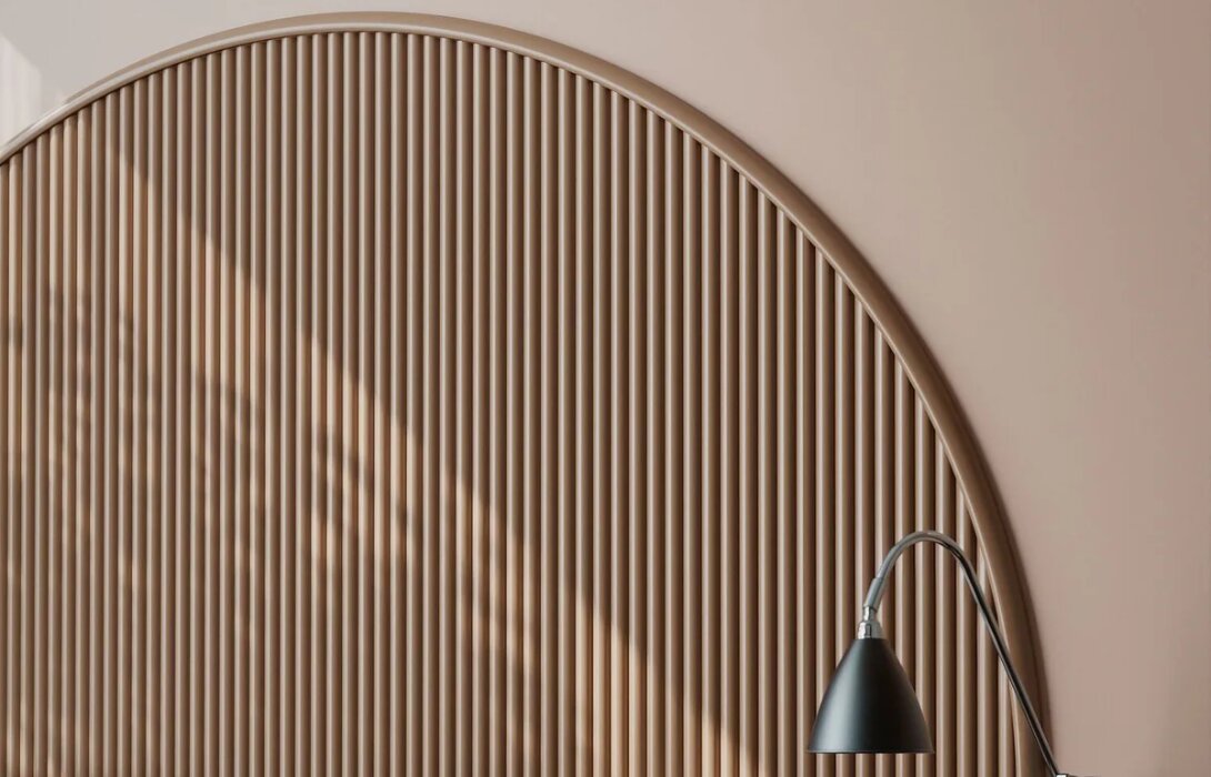 Flexibele sierlijst omlijst een boogvormig hoofdbord van houten latten boven een bed, met een leeslamp
