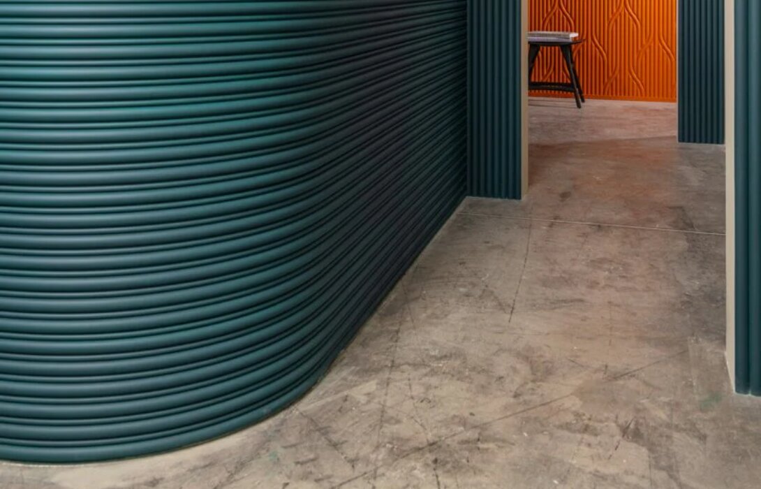Donkergroene gebogen wand met ribbelpanelen die om een ronding lopen, met een flexibele plint langs de vloer