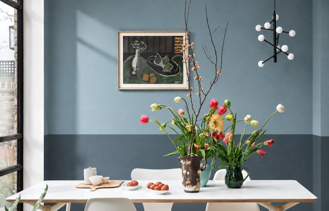 Eetkamer met een half geverfde muur in twee blauwtinten: lichter grijsblauw boven, dieper blauwgrijs onder.