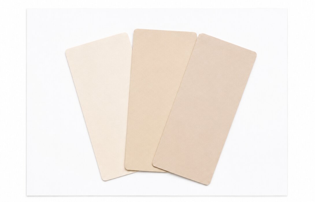 Drie beige kleurstalen waaiervormig op een vel zuiver wit papier, waardoor de warme en koele ondertonen zichtbaar worden.