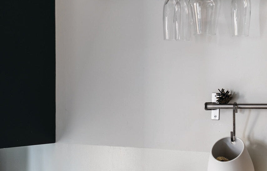 Koele, strakke keukenwand in Farrow & Ball Strong White (2001) naast een zwart keukenfront, met glazen en een kraan