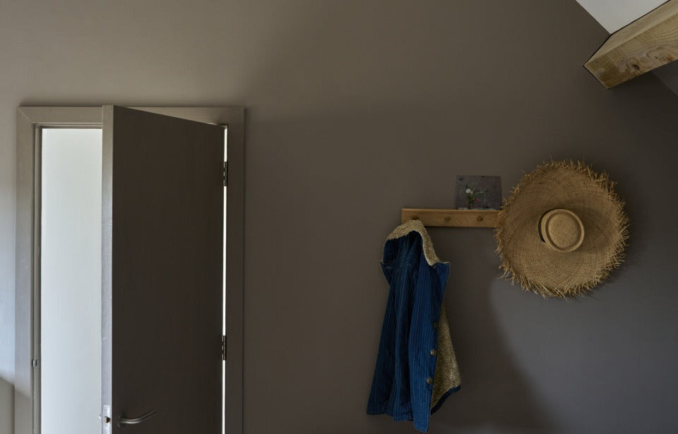 Diepe taupe zolderkamer met Farrow & Ball Charleston Gray (243) op de wand en All White (2005) op de nok, met houten kapstok, strohoed en linnen jas