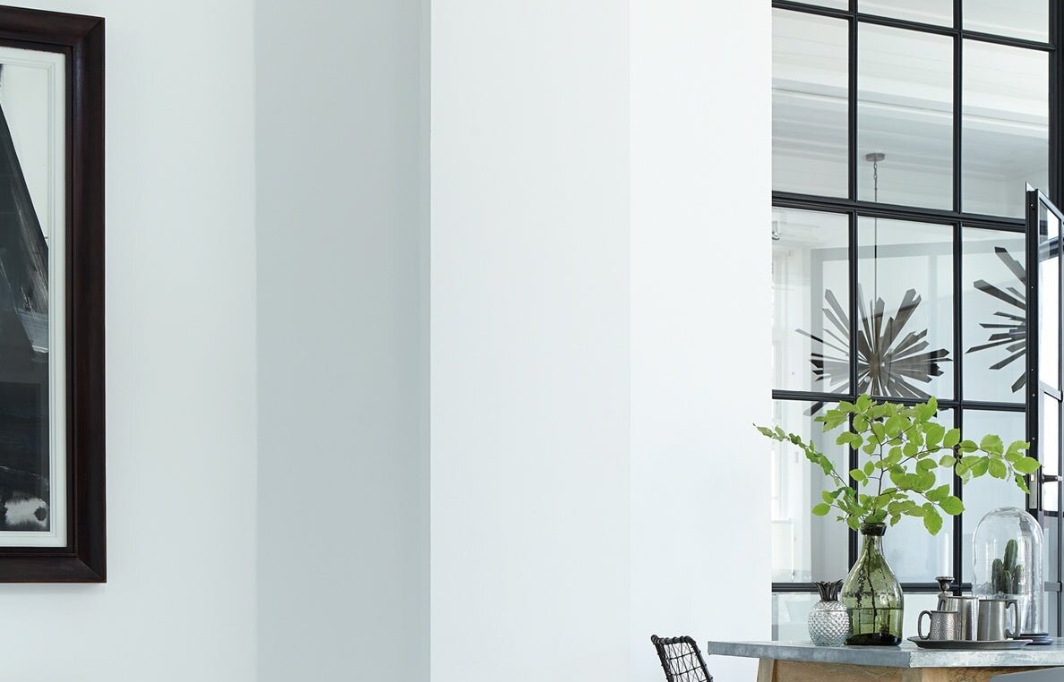 Heldere, open ruimte in Little Greene Loft White (222) met wit plafond en wanden, een zwart omlijste glaswand en een eettafel op de achtergrond