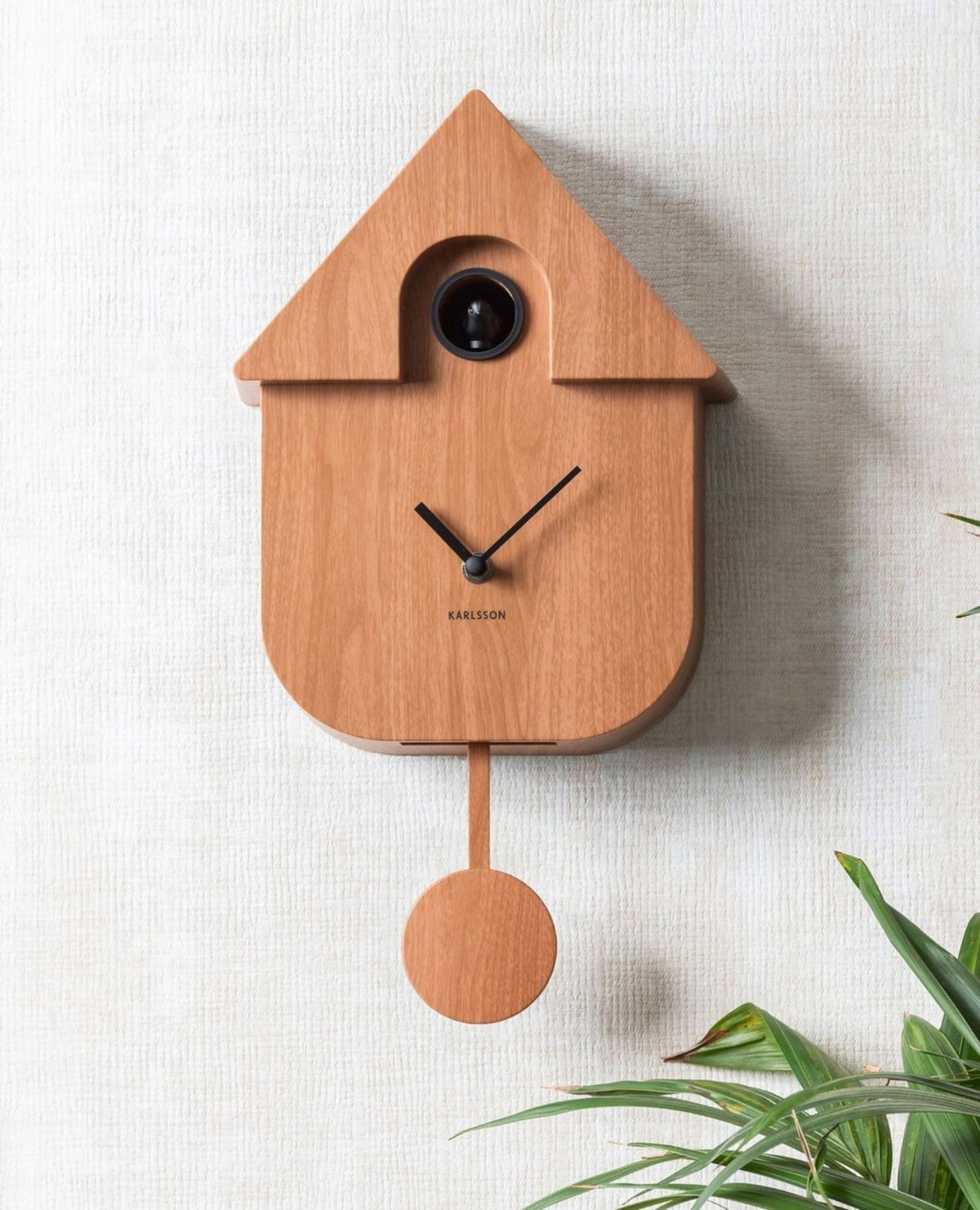 Karlsson koekoeksklok Modern Cuckoo, donker hout print, sfeerfoto: aan lichte wand naast palmbladeren