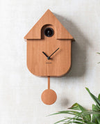 Karlsson koekoeksklok Modern Cuckoo, donker hout print, sfeerfoto: aan lichte wand naast palmbladeren