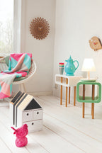 Karlsson wandklok Sunflower MDF, hout finish, sfeerfoto: aan witte wand in kinderkamer met rieten stoel en gekleurde plaid