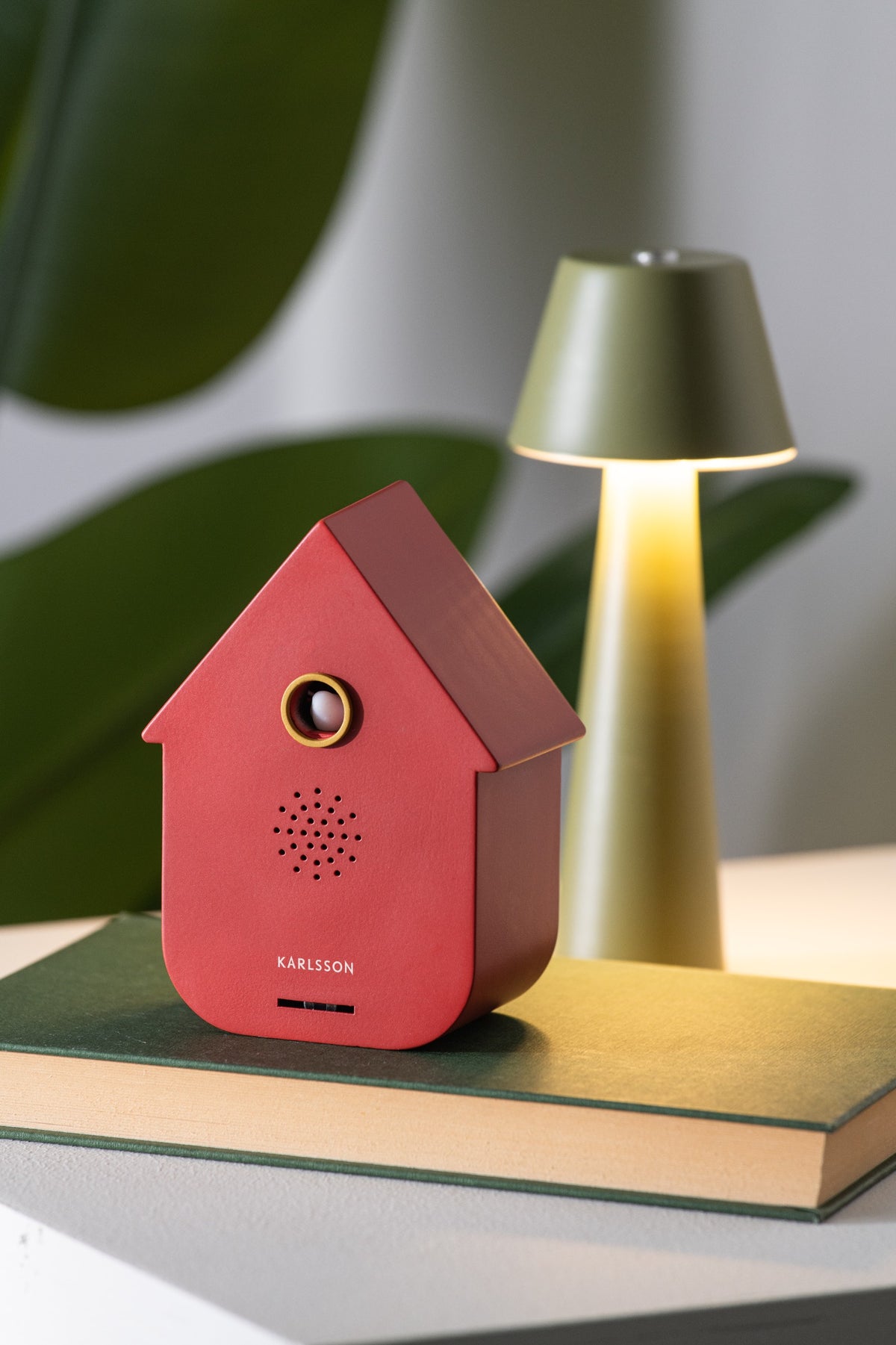 Karlsson vogelhuisje met geluid (soundbox) Modern Cuckoo, rood, sfeerfoto: op groen boek naast tafellamp en plant