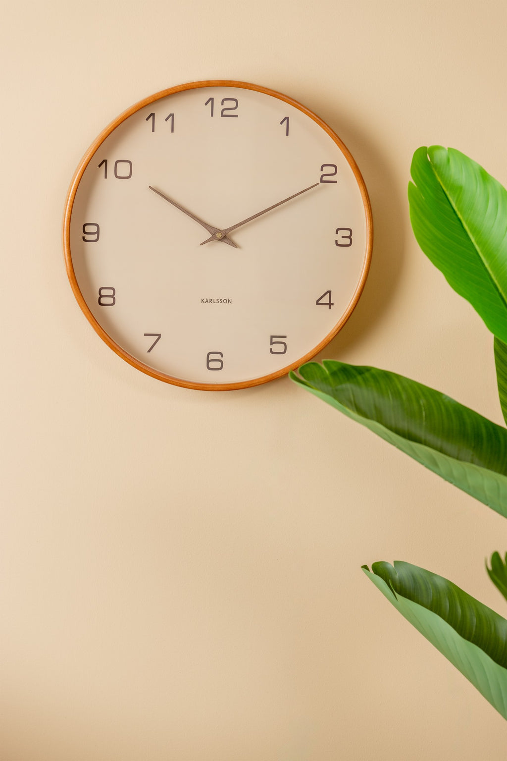 Karlsson wandklok Acento, bruin, sfeerfoto: aan beige muur naast groene plant
