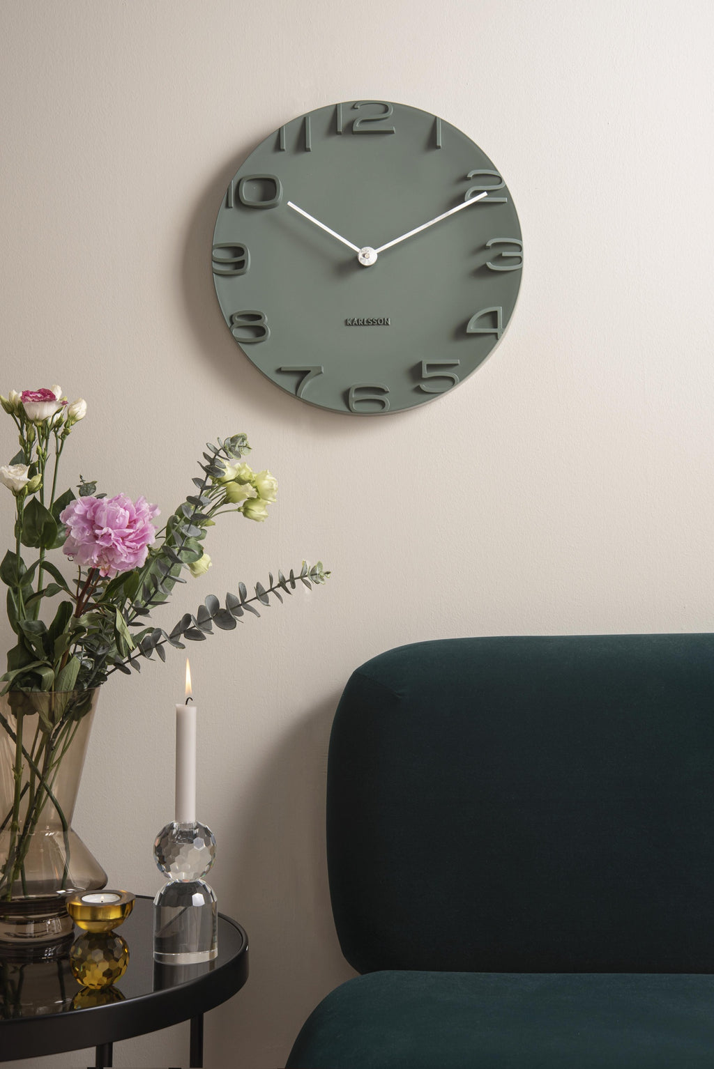 Karlsson wandklok On The Edge, jungle groen met chromen wijzers, sfeerfoto: aan lichte wand boven groene velours fauteuil