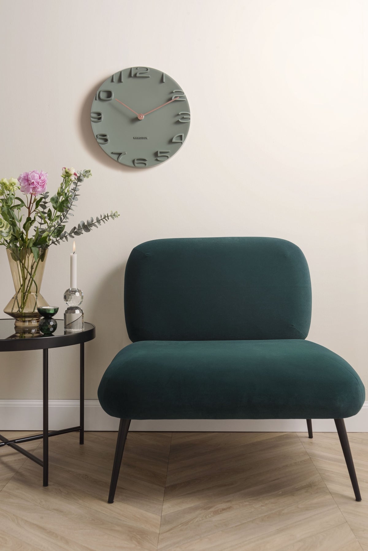 Karlsson wandklok On The Edge, jungle groen met chromen wijzers, sfeerfoto: aan lichte wand boven groene fauteuil