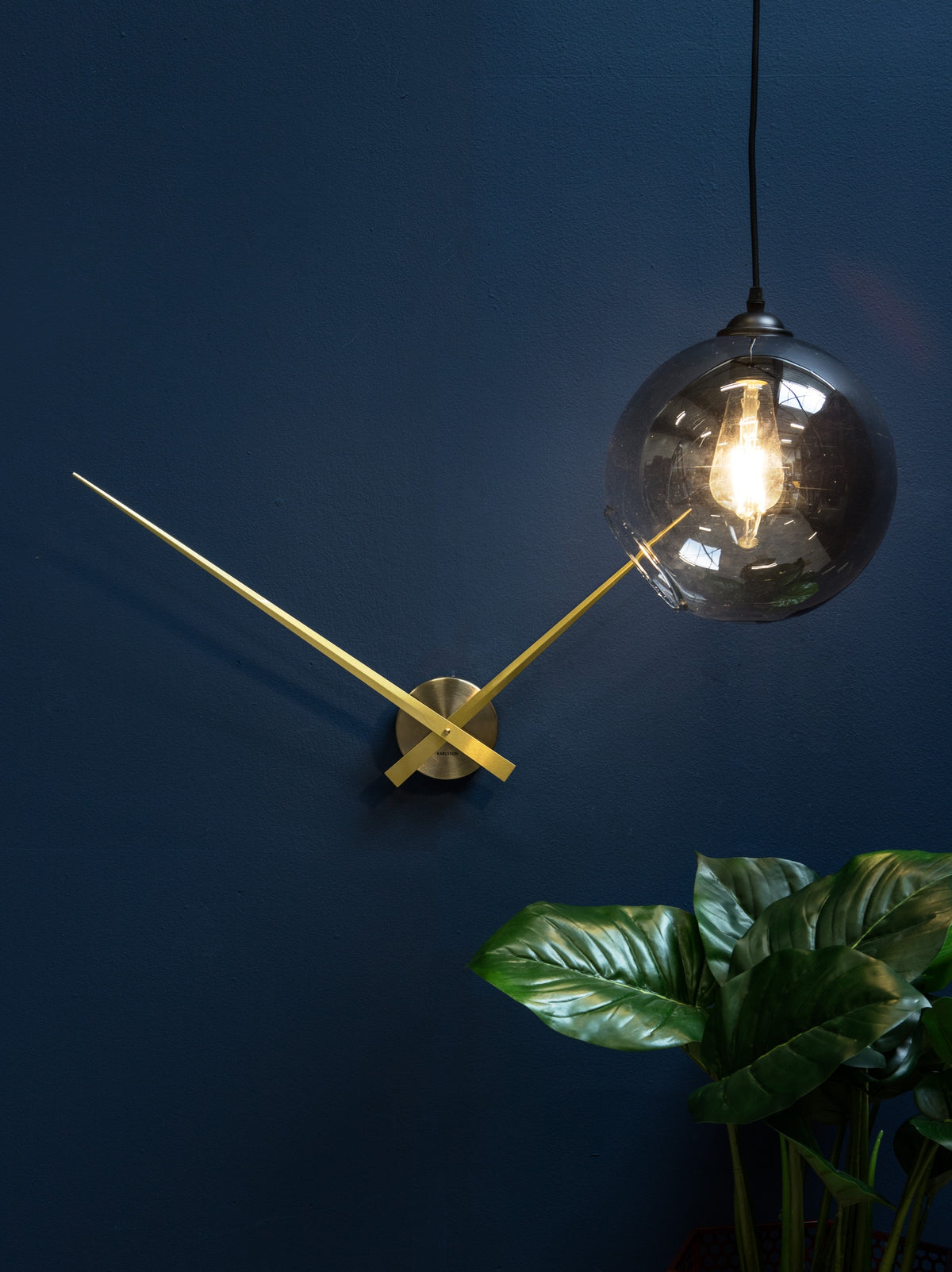 Karlsson wandklok Little Big Time, goud verguld, sfeerfoto: aan donkerblauwe muur naast hanglamp en plant