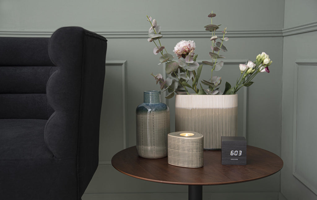Karlsson wekker Mini Cube, zwart fineer, witte led, sfeerfoto: op ronde bijzettafel naast vazen en bloemen