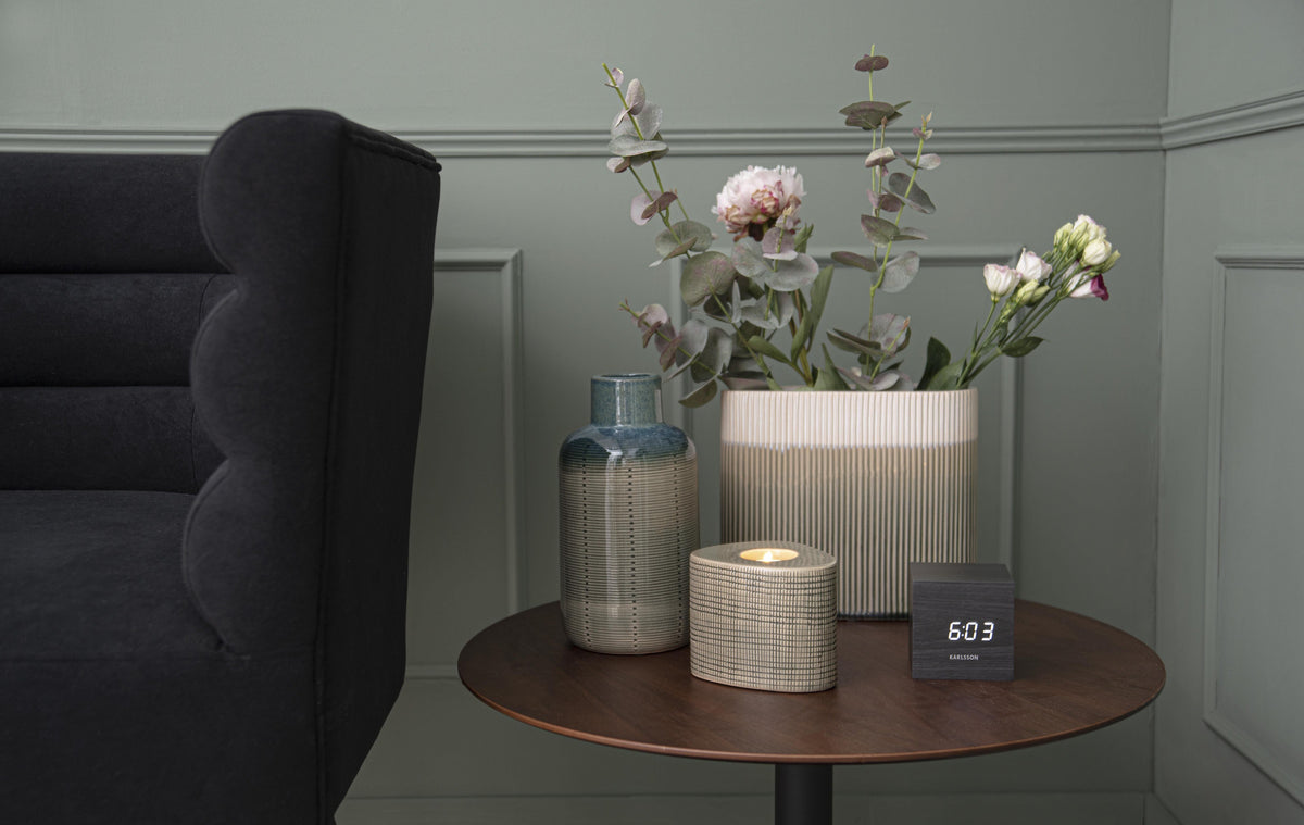 Karlsson wekker Mini Cube, zwart fineer, witte led, sfeerfoto: op ronde bijzettafel naast vazen en bloemen