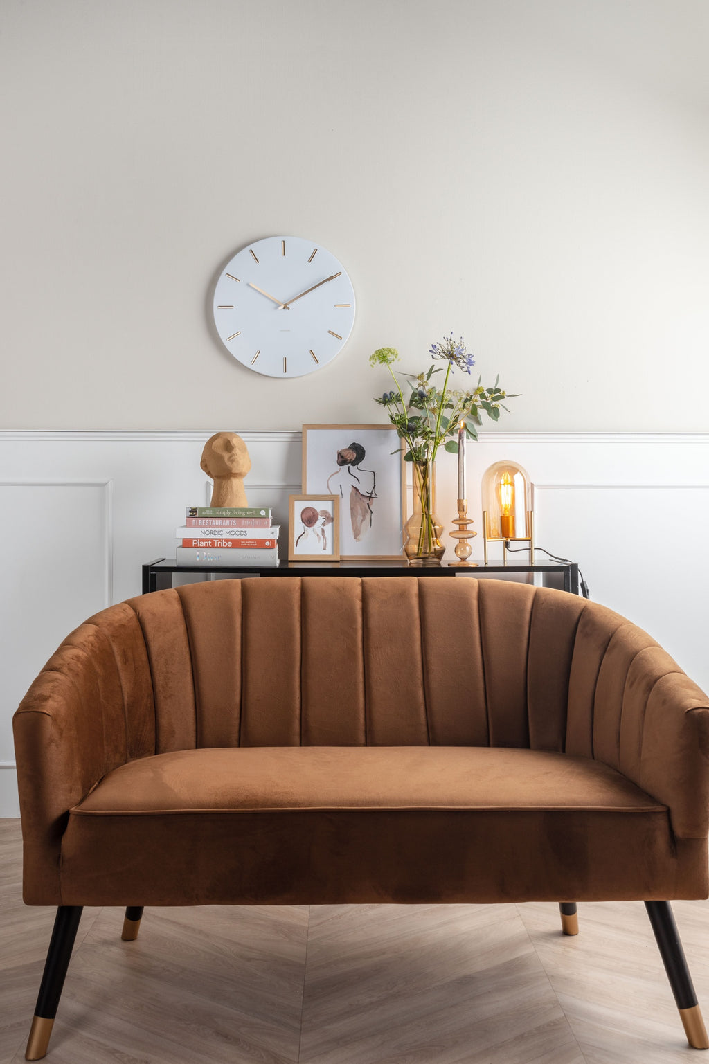 Karlsson wandklok Charm, wit, sfeerfoto: boven bruine velours bank en zwart sidetable met boeken, buste en bloemen