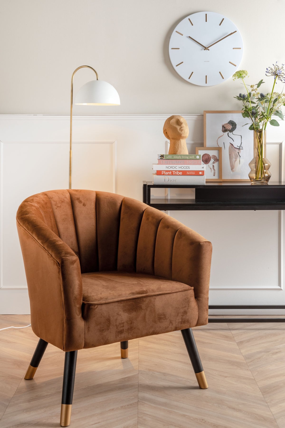 Karlsson wandklok Charm, wit, sfeerfoto: boven bruine velours fauteuil en sidetable met boeken en bloemen, witte booglamp