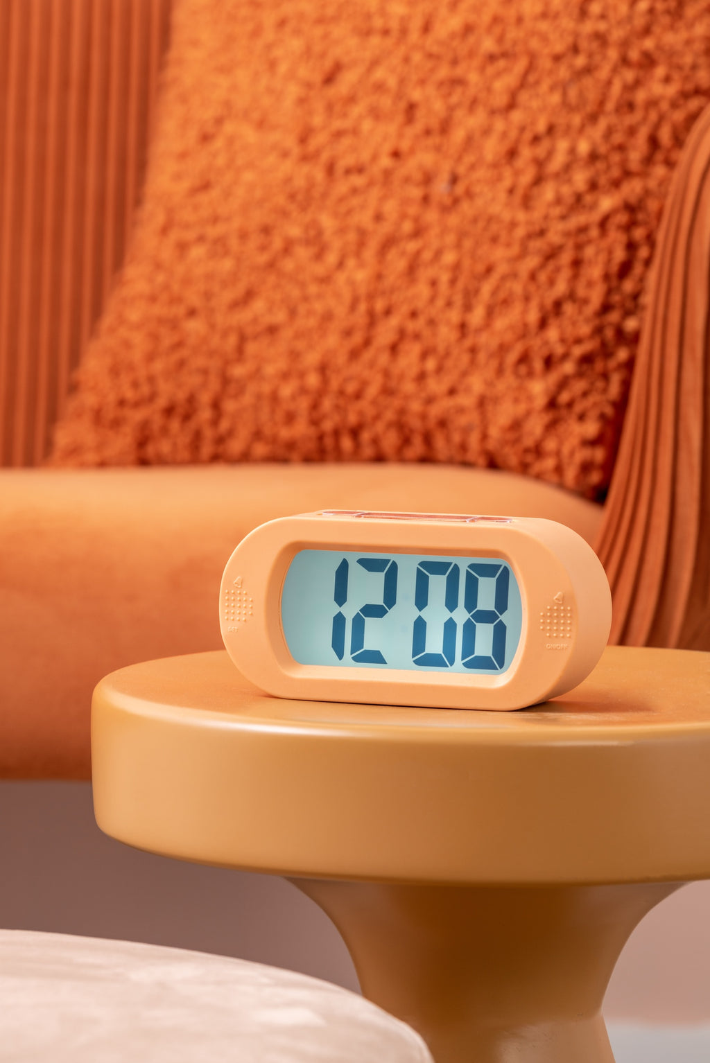 Karlsson wekker Gummy Rubberized, oranje, sfeerfoto: op gele bijzettafel voor oranje bank, display toont 12:08