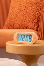 Karlsson wekker Gummy Rubberized, oranje, sfeerfoto: op gele bijzettafel voor oranje bank, display toont 12:08