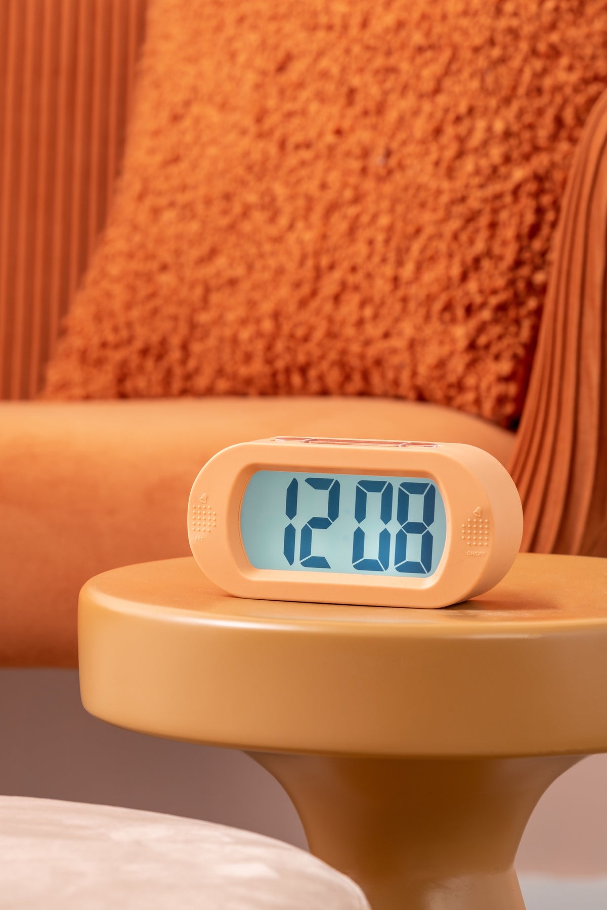 Karlsson wekker Gummy Rubberized, oranje, sfeerfoto: op gele bijzettafel voor oranje bank, display toont 12:08