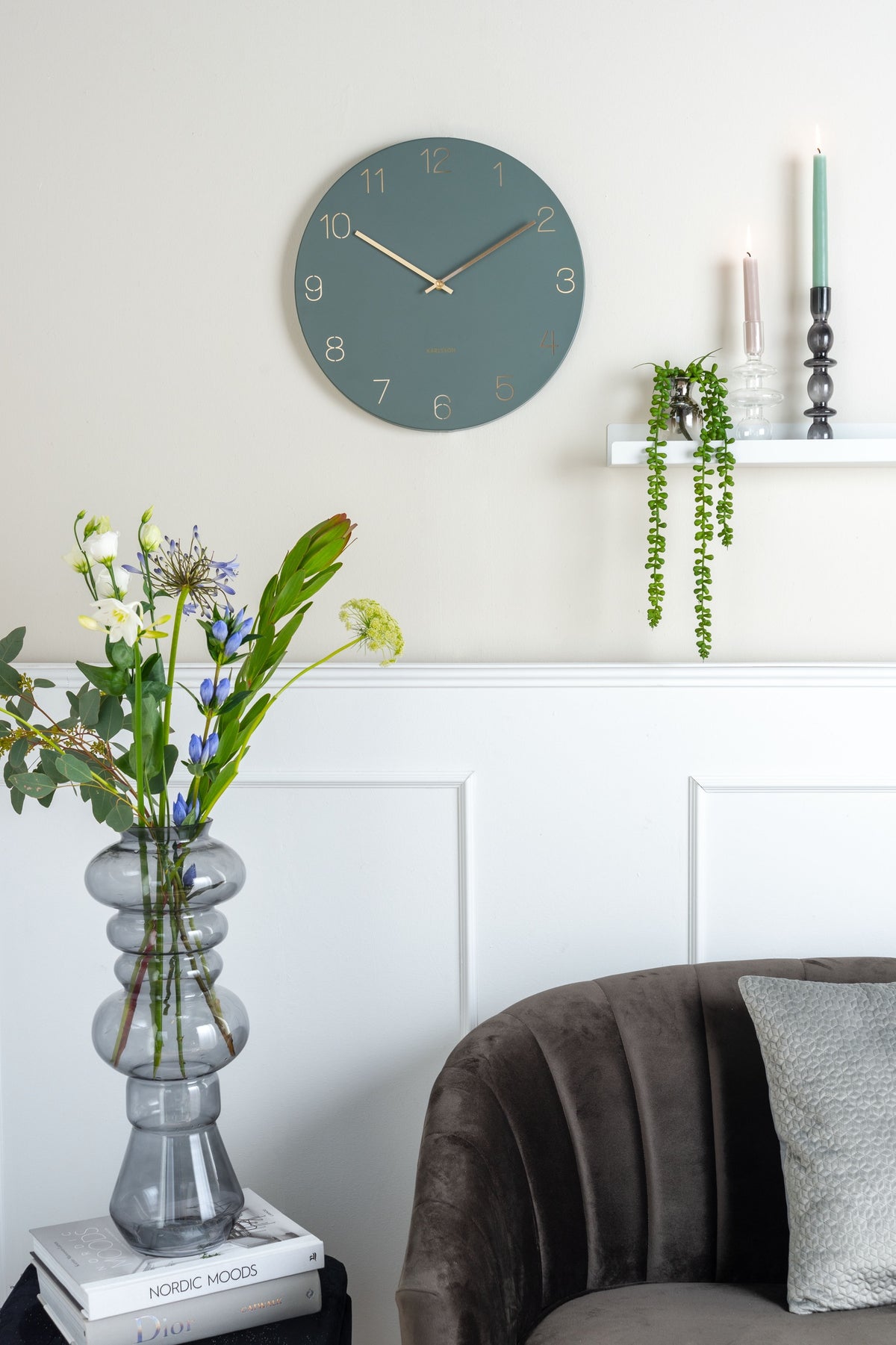 Karlsson wandklok Charm, gegraveerde nummers, jungle groen, sfeerfoto: aan lichte wand met lambrisering, bloemen