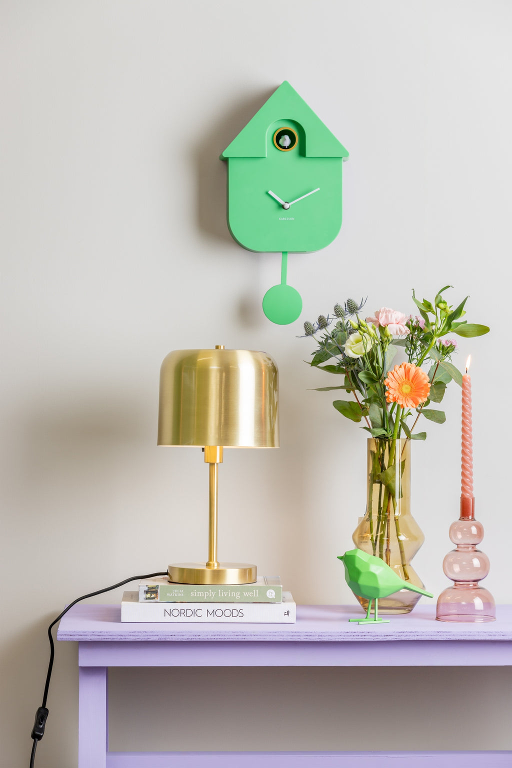Karlsson koekoeksklok Modern Cuckoo, fel groen abs, sfeerfoto: boven lila sidetable met gouden lamp en bloemen