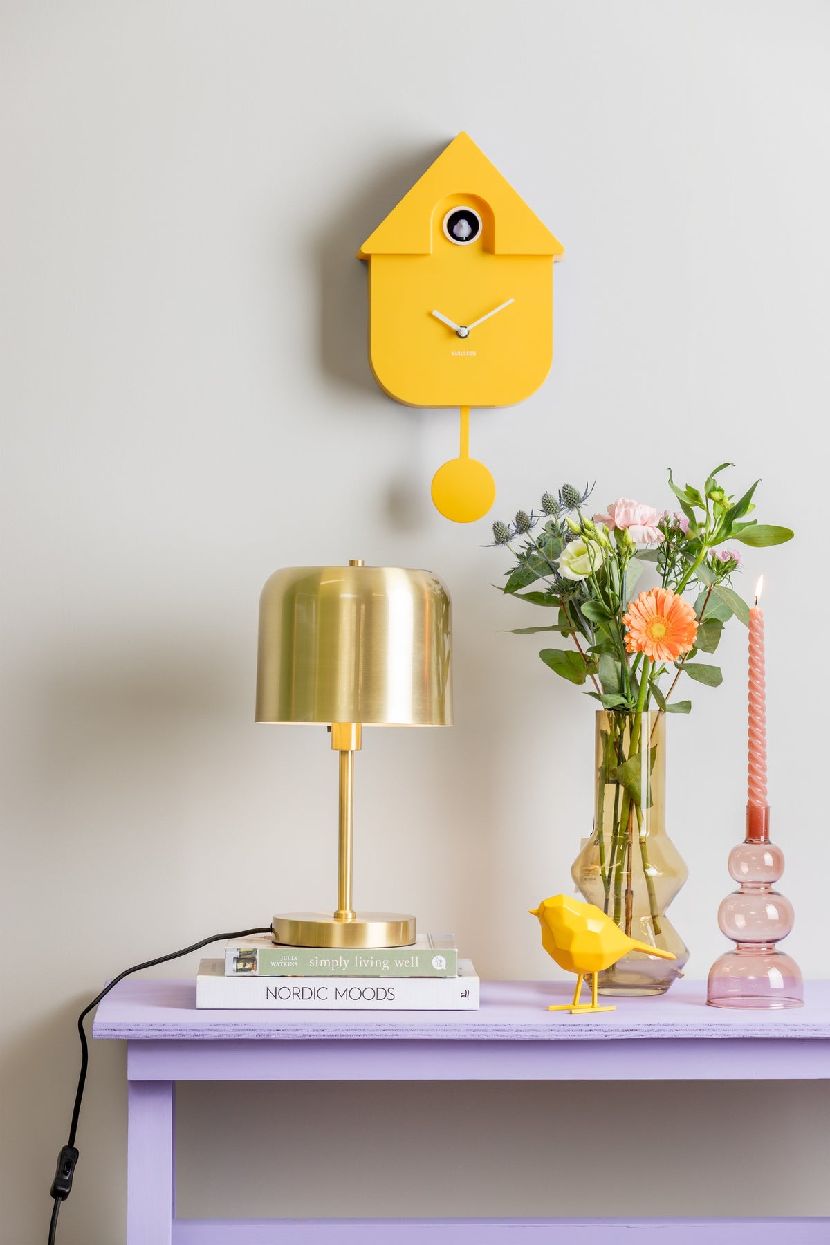 Karlsson koekoeksklok Modern Cuckoo, fel geel abs, sfeerfoto: boven lila sidetable met gouden lamp en bloemen