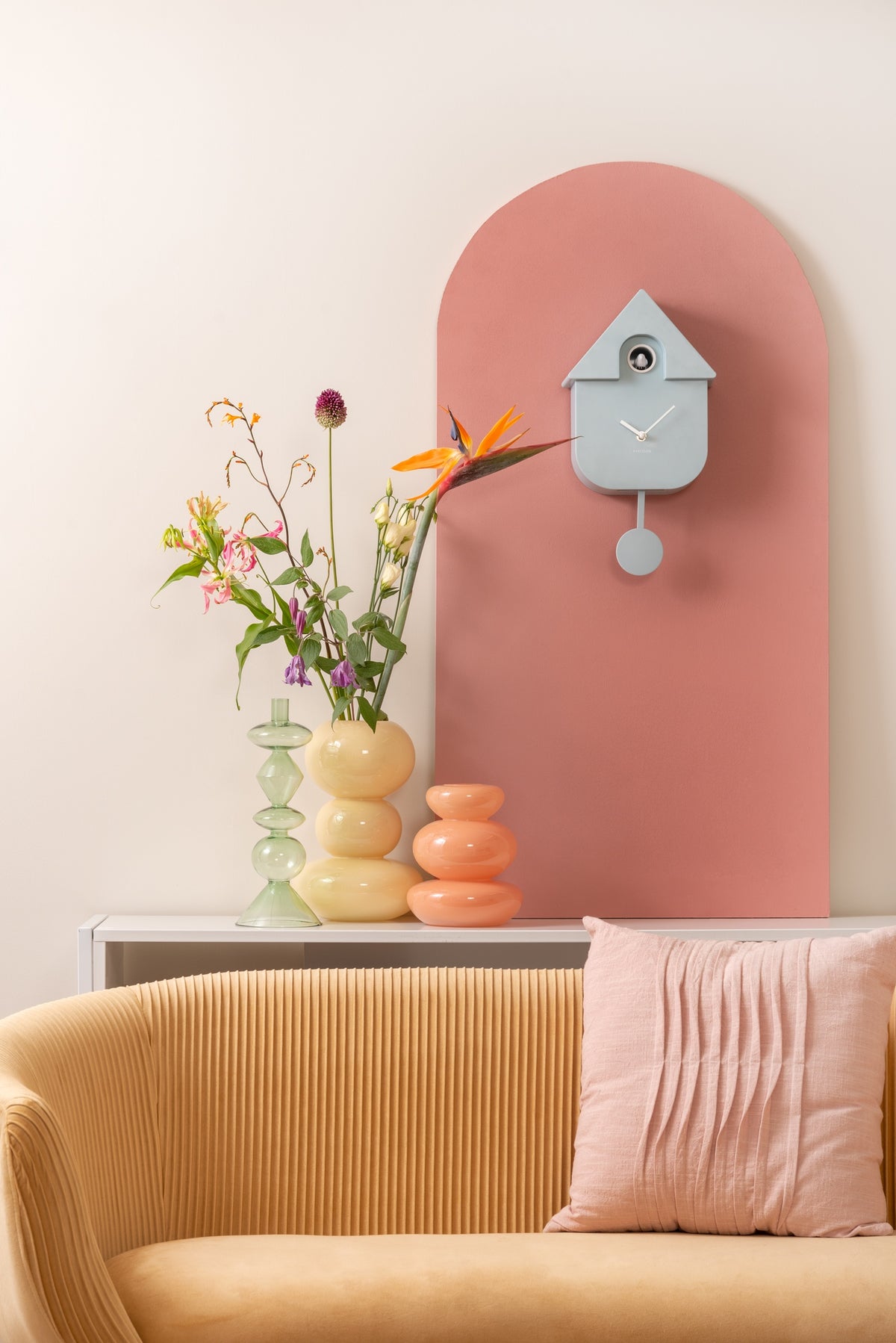 Karlsson koekoeksklok Modern Cuckoo, lichtblauw abs, sfeerfoto: op roze boogpaneel boven gele bank met vazen en bloemen