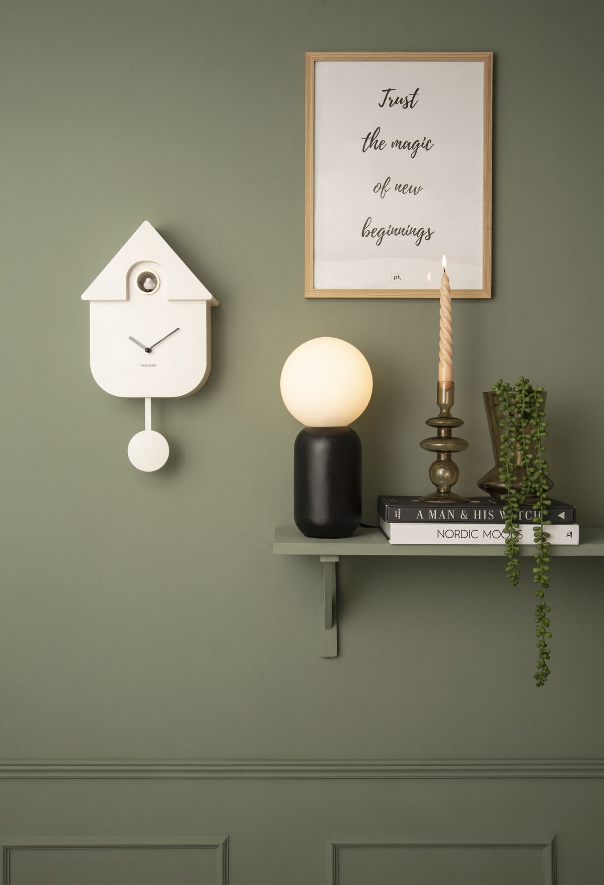 Karlsson koekoeksklok Modern Cuckoo, wit, sfeerfoto: aan groene wand naast wandplank met bollamp, kaars en poster