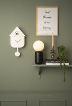 Karlsson koekoeksklok Modern Cuckoo, wit, sfeerfoto: aan groene wand naast wandplank met bollamp, kaars en poster