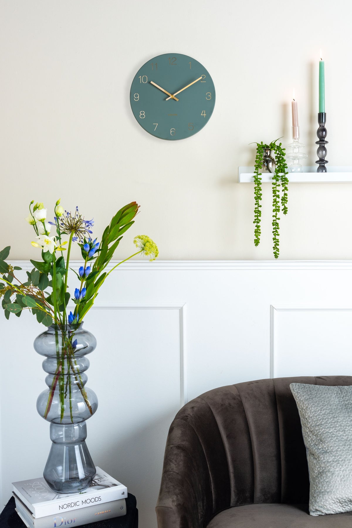 Karlsson wandklok Charm Small, gegraveerde cijfers, jungle groen, sfeerfoto: aan lichte wand met lambrisering, bloemen
