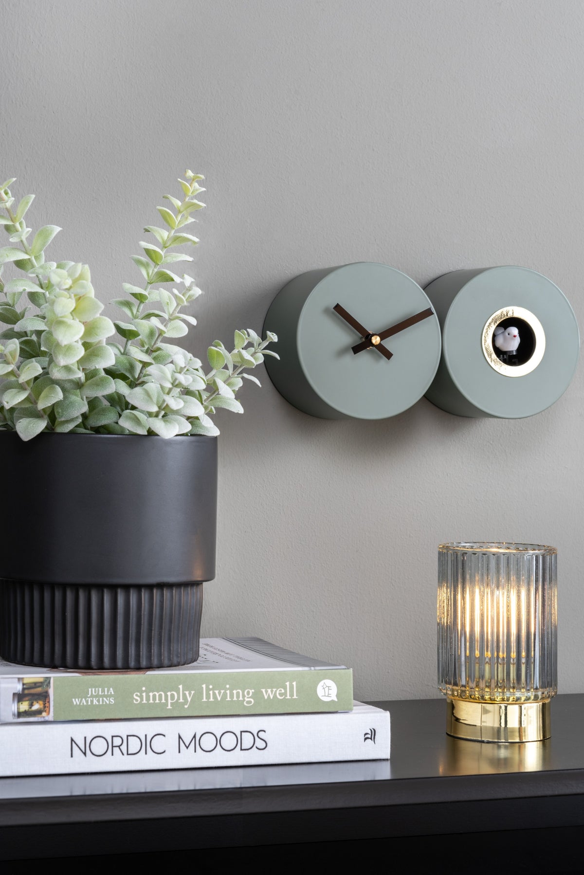 Karlsson koekoeksklok Duo Cuckoo, mat jungle groen, sfeerfoto: aan grijze wand naast plant, boeken en geribbelde lamp