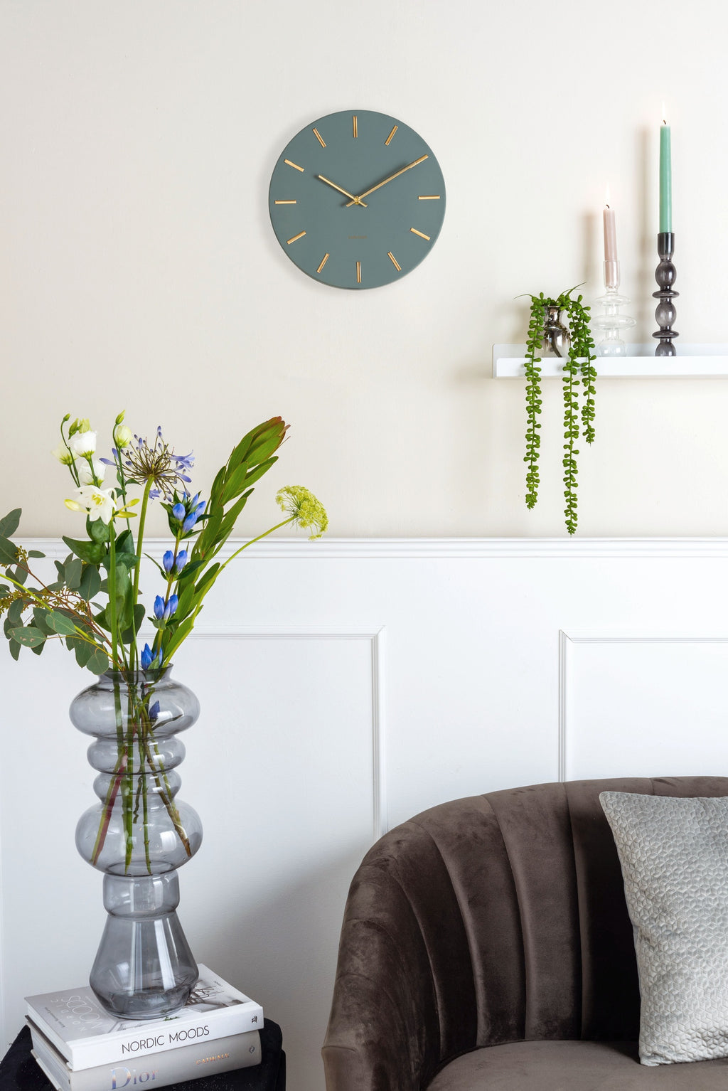 Karlsson wandklok Charm Small, groen, sfeerfoto: aan crème wand boven wandplank met hangplant en kandelaars