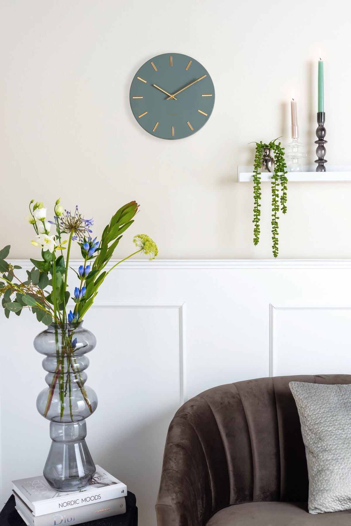 Karlsson wandklok Charm Small, groen, sfeerfoto: aan crème wand boven wandplank met hangplant en kandelaars