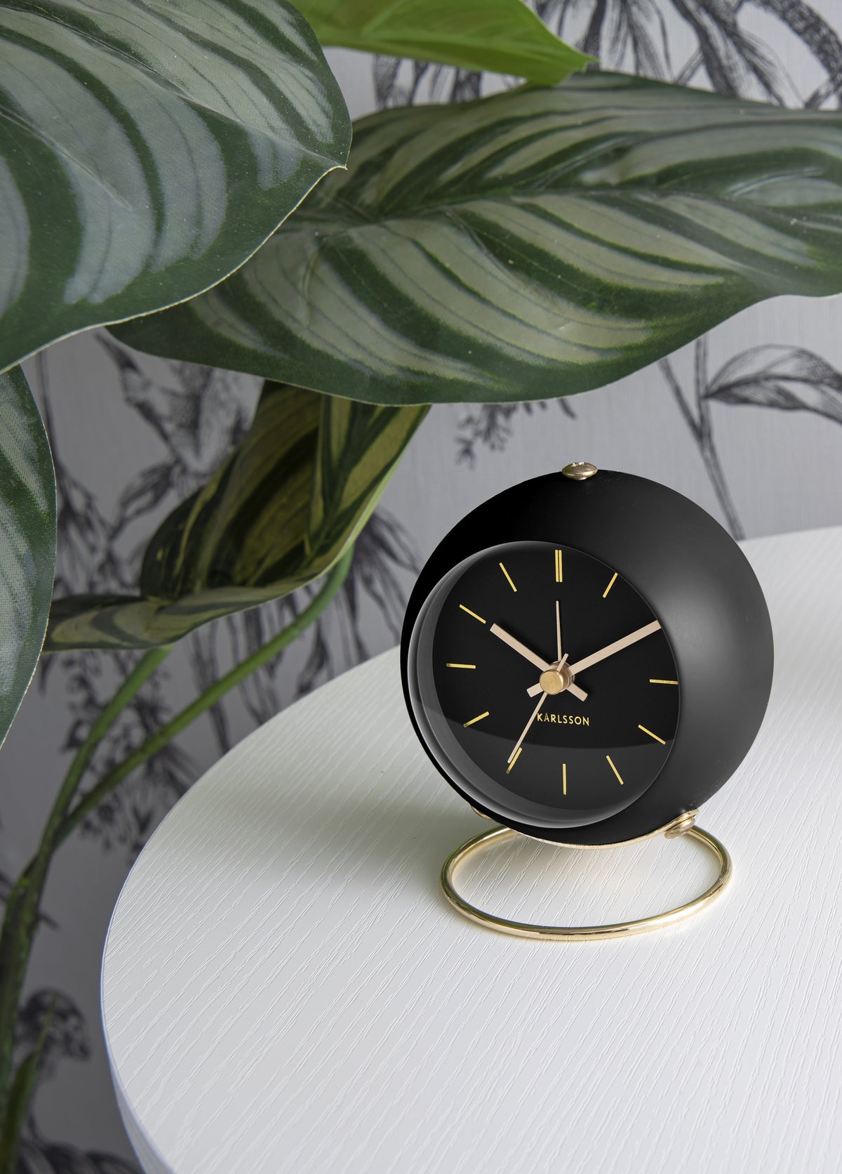 Karlsson wekker Globe Armando Breeveld, zwart, sfeerfoto: op wit tafeltje voor plant en botanisch behang