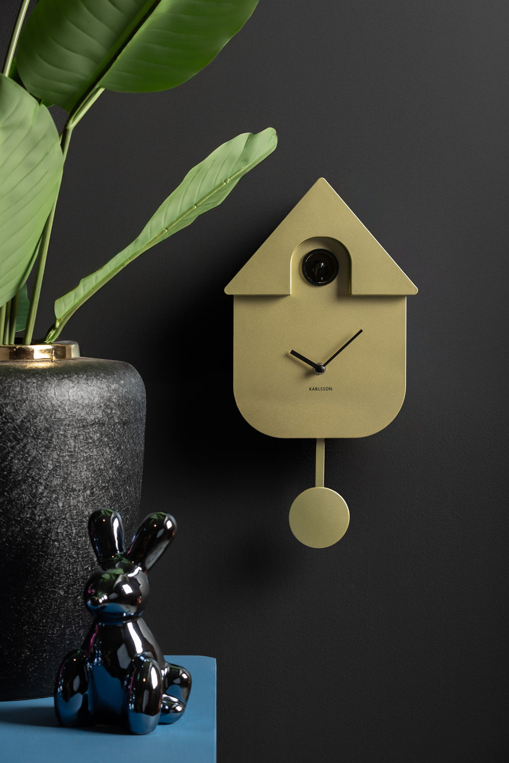 Karlsson koekoeksklok Modern Cuckoo, goud abs metallic, sfeerfoto: aan donkere muur naast plant en glanzend konijn