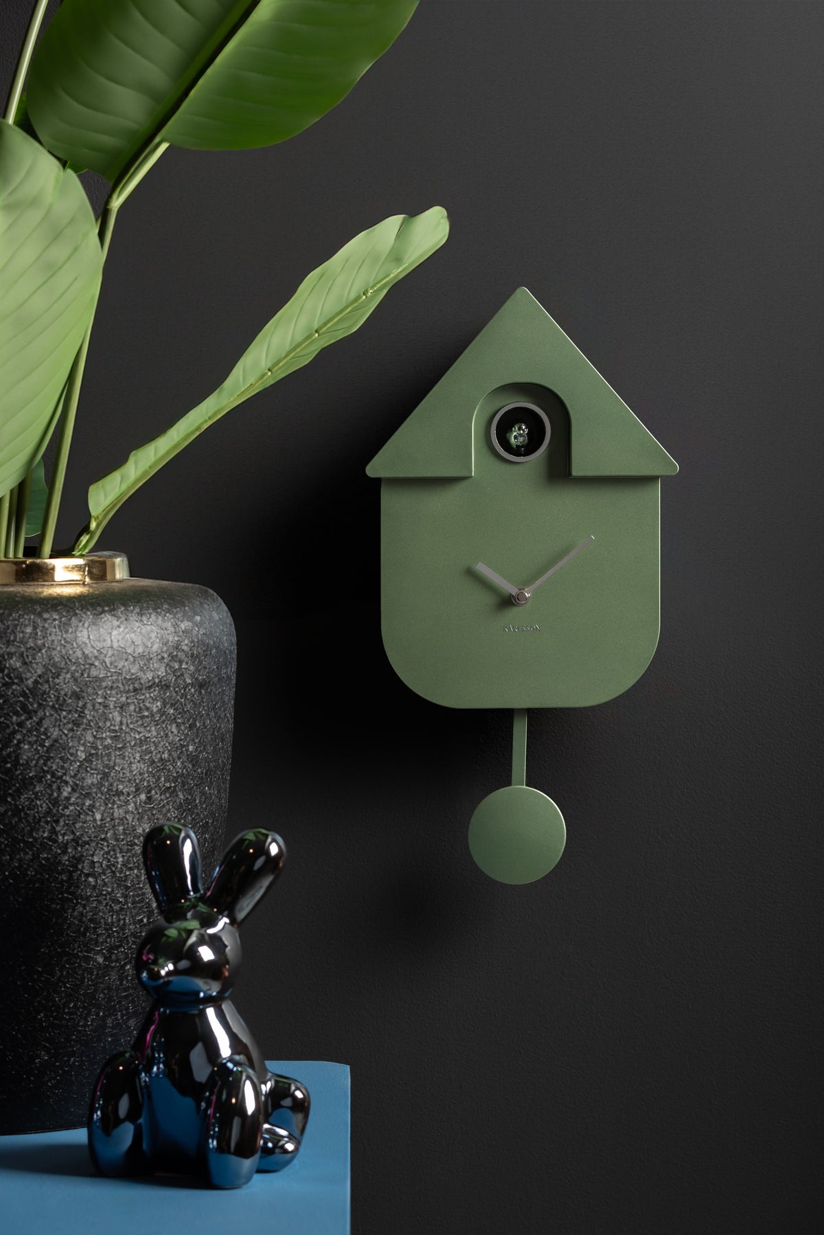 Karlsson koekoeksklok Modern Cuckoo, jungle groen abs metallic, sfeerfoto: aan donkere muur naast plant en glanzend konijn