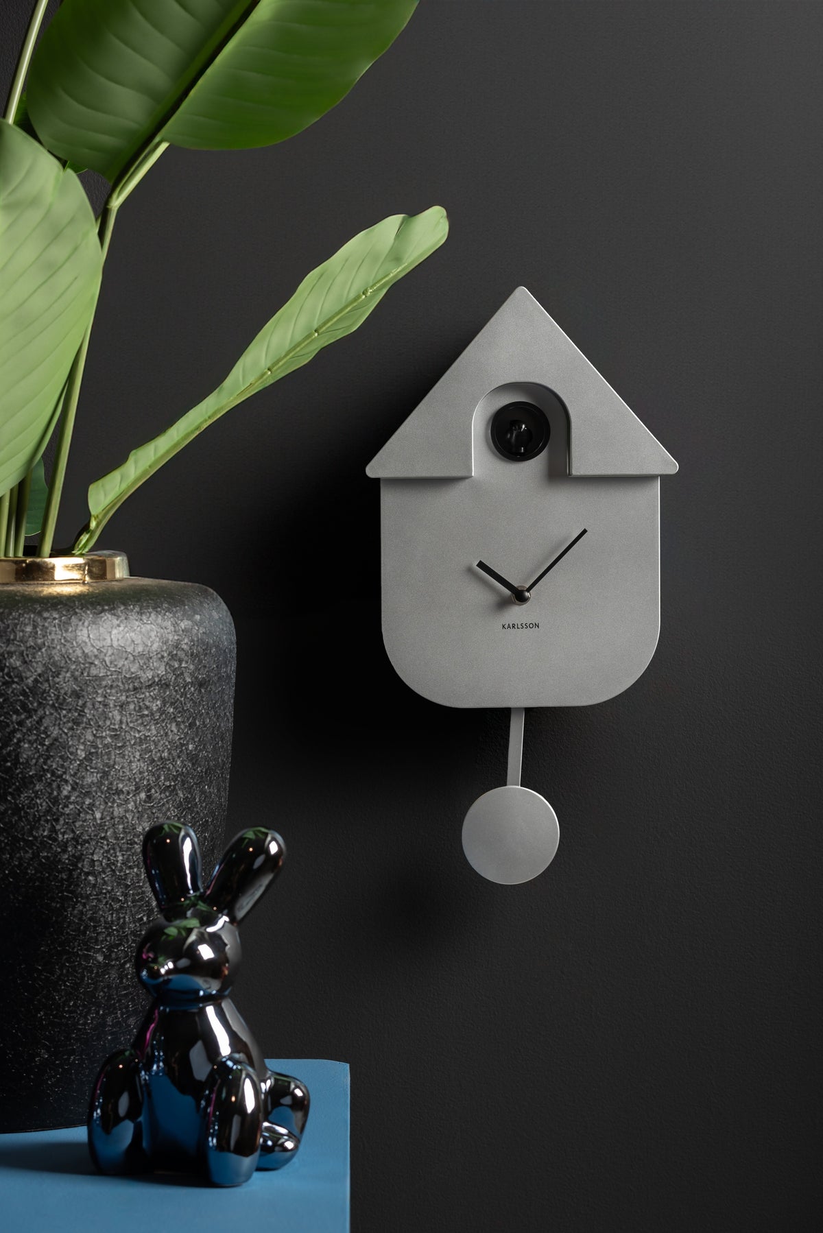 Karlsson koekoeksklok Modern Cuckoo, zilver abs metallic, sfeerfoto: aan donkere muur naast plant en glanzend konijn