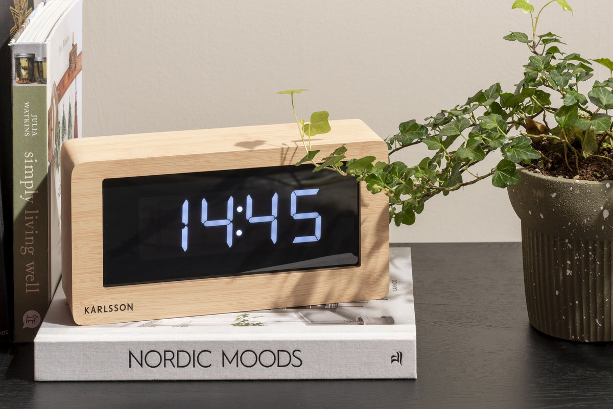 Karlsson tafelklok Boxed Led, licht hout fineer, sfeerfoto: op boek Nordic Moods naast plant, display toont 14:45