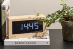 Karlsson tafelklok Boxed Led, licht hout fineer, sfeerfoto: op boek Nordic Moods naast plant, display toont 14:45