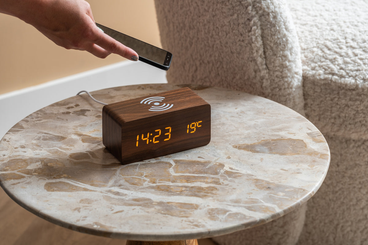 Karlsson wekker Block, donker hout fineer, witte led, draadloze oplader, sfeerfoto: hand legt telefoon op de wekker
