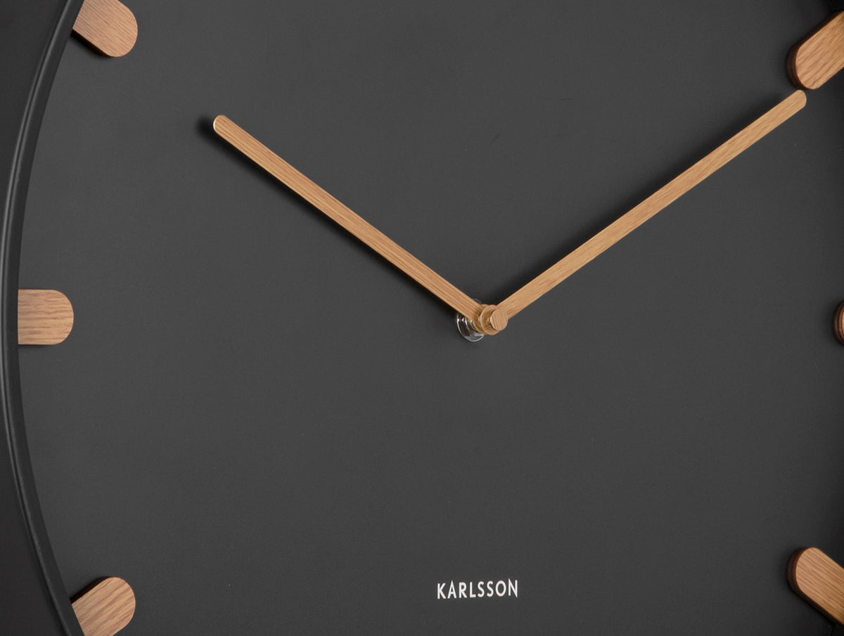 Karlsson wandklok Grace, zwart, detail: houten wijzers en houten streepjes op zwarte wijzerplaat, Karlsson-logo