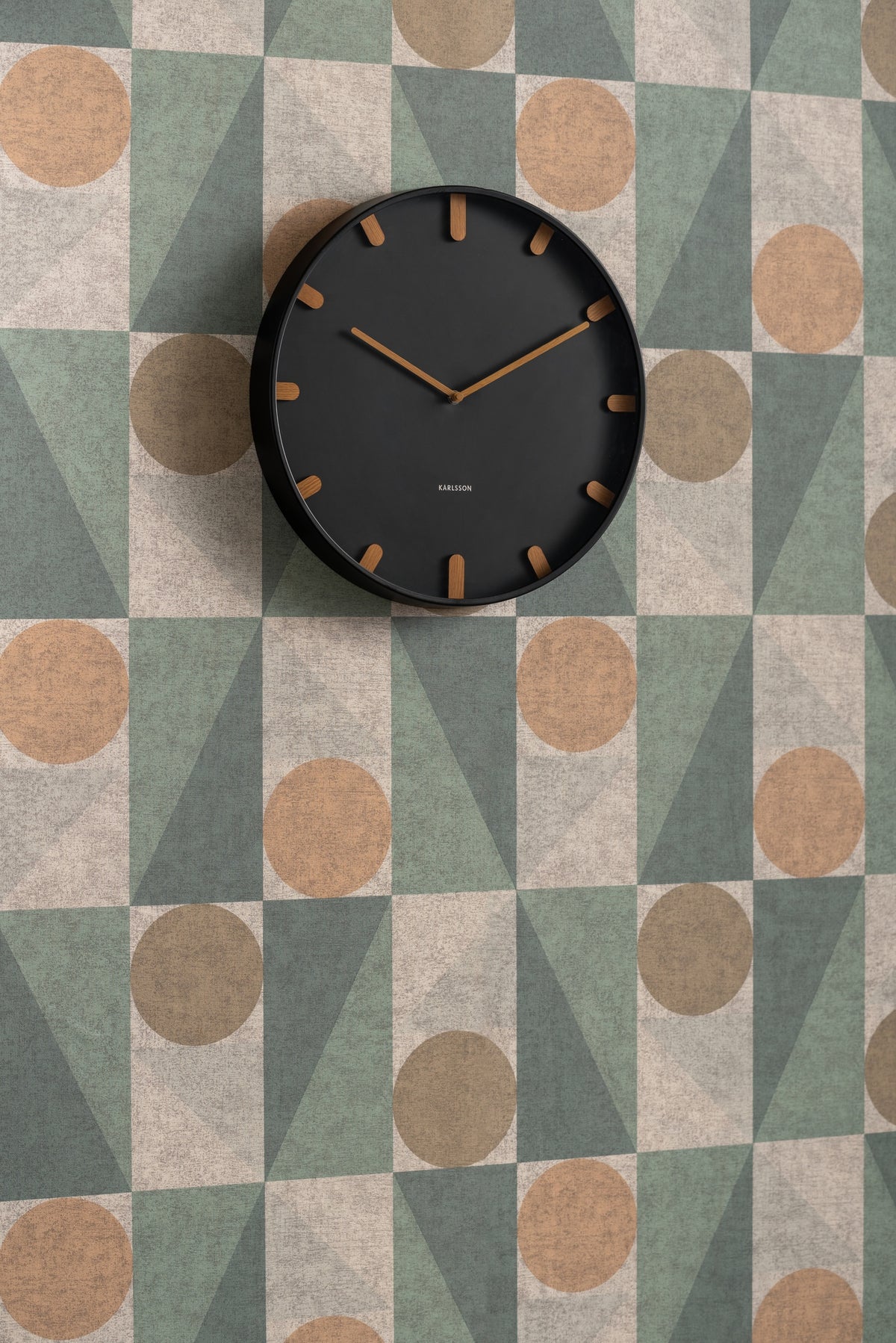 Karlsson wandklok Grace, zwart, sfeerfoto: aan wand met geometrisch behang in groen, beige en terracotta