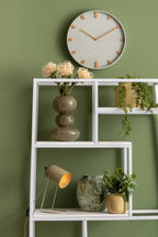 Karlsson wandklok Grace, groen, sfeerfoto: aan groene wand boven wit stalen wandrek met vazen, planten en lampje