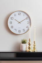 Karlsson wandklok Elegance Glow, wit, sfeerfoto: aan witte muur boven zwart dressoir met gouden kandelaars en plantje