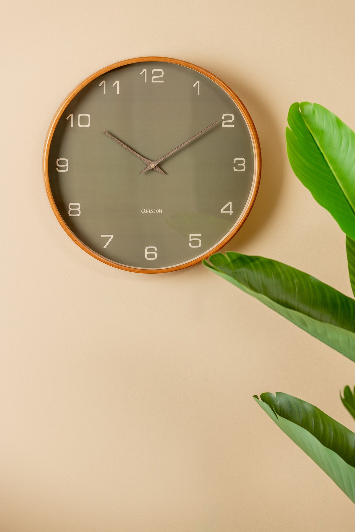 Karlsson wandklok Acento, groen, sfeerfoto: aan beige muur naast groene plant