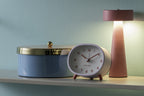 Karlsson wekker Cheeky Oval, zachtpaars, sfeerfoto: op plank naast blauwe opbergdoos en roze lamp