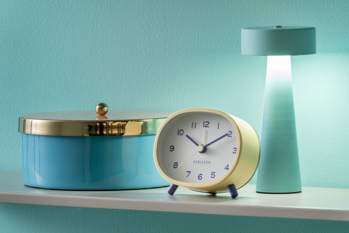 Karlsson wekker Cheeky Oval, zachtgeel, sfeerfoto: op plank naast blauwe opbergdoos en mintgroene lamp