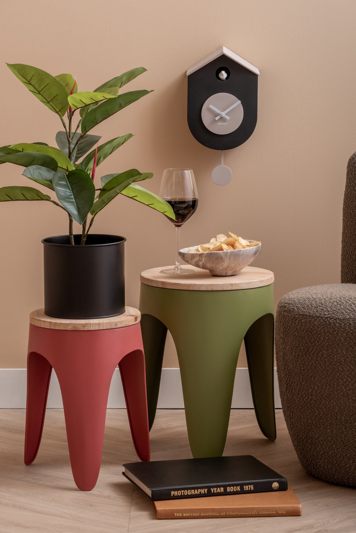Karlsson koekoeksklok Grato Cuckoo, zwart en warmgrijs, sfeerfoto: boven krukjes met plant, wijnglas en fauteuil