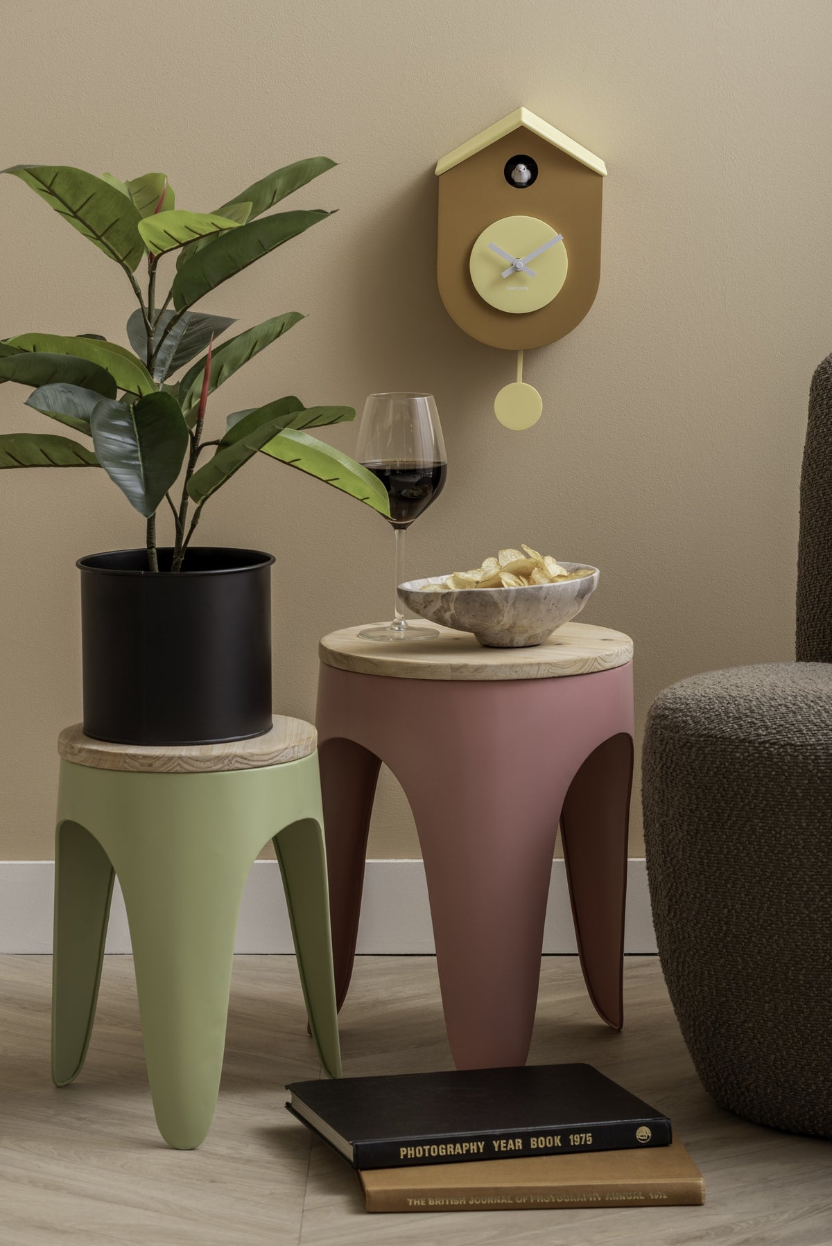 Karlsson koekoeksklok Grato Cuckoo, okergeel en zachtgeel, sfeerfoto: boven krukjes met plant, wijnglas en fauteuil